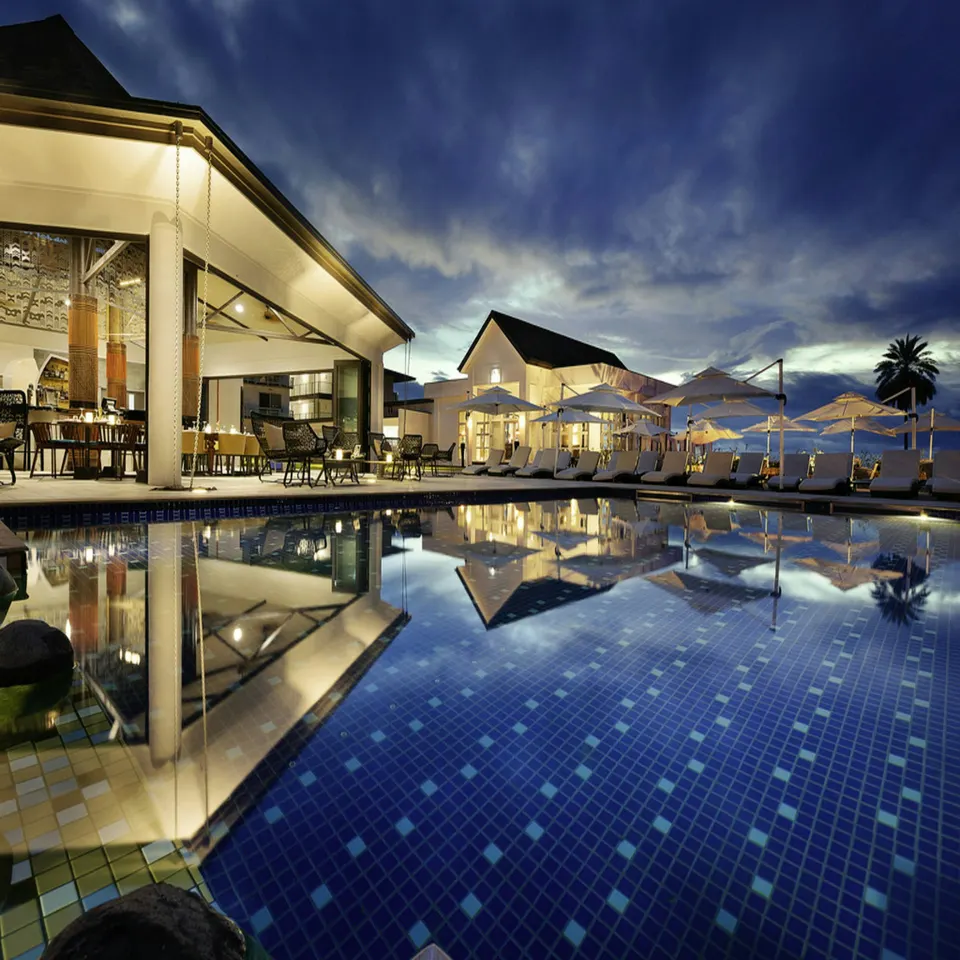 Resort buildings and a swimming pool reflected in still water at dusk